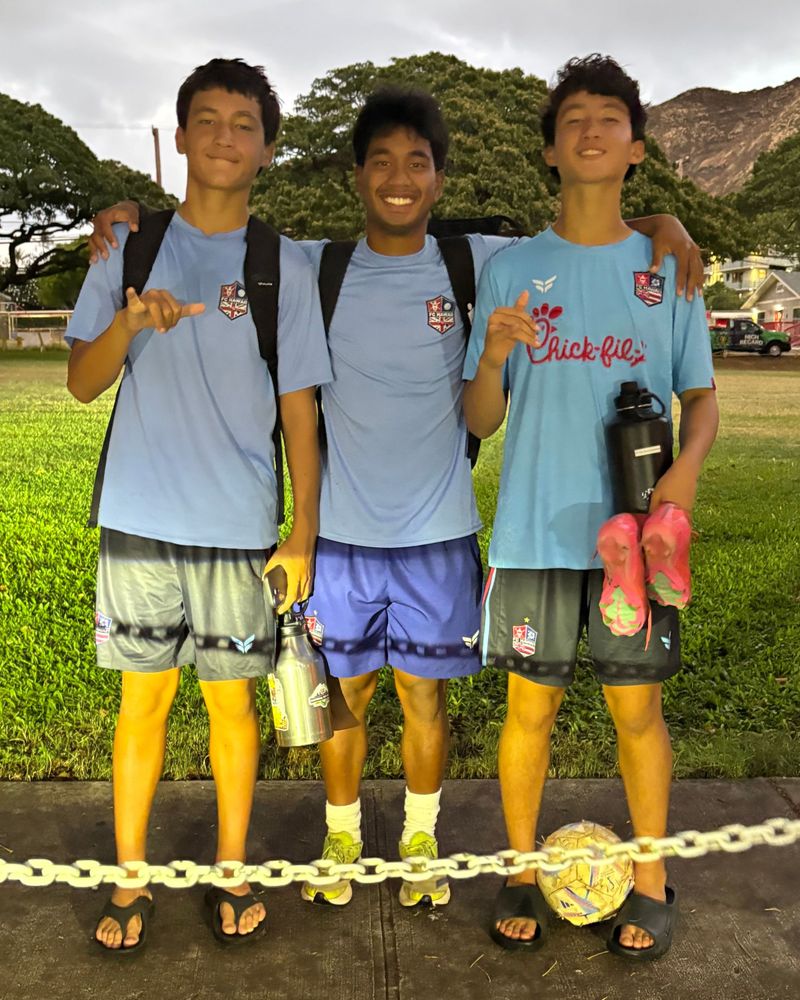 Coach Joe smiling with two young players at a park, a soccer ball at their feet